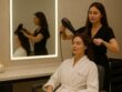 Luxury hair salon experience at Villa 8 Ladies Salon & Spa in Jumeirah, Dubai. A woman in a white robe with the Villa 8 logo enjoys a professional blow-dry in an elegant, softly lit salon with illuminated mirrors and refined decor.