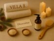 Festive spa flatlay at Villa 8 Ladies Salon & Spa in Jumeirah, Dubai, featuring pine branches, wooden wellness tools, a candle, rolled towels, massage oil, and holiday accents arranged in a warm, elegant setting