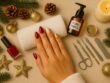 Festive holiday manicure with deep red and gold chrome nails displayed on a feminine hand, surrounded by nail tools, pine branches, gold ornaments, and candlelight in a luxury spa setting at Villa 8 in Jumeirah, Dubai.